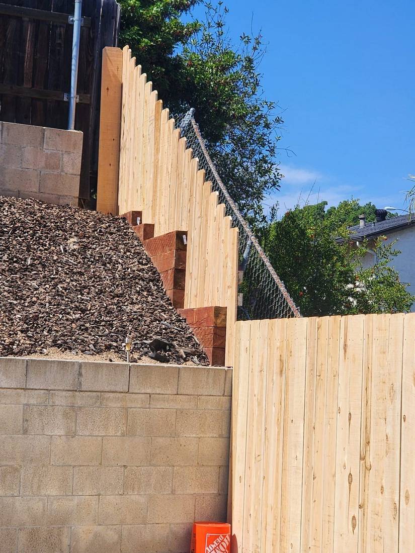 Stepped wood fence following the slope of the property, over a block wall — Benitez Tree Service